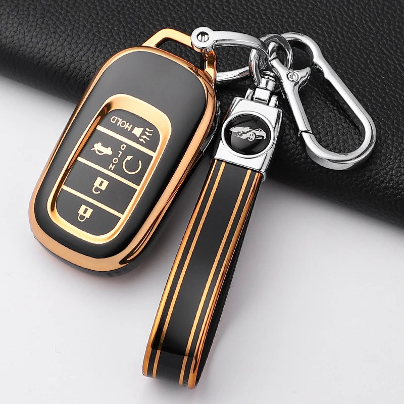 A close-up of a gold and black Honda key fob cover with a leather strap and metal keyring attached.