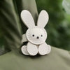 A small, white, embroidered bunny charm attached to a light green fabric.