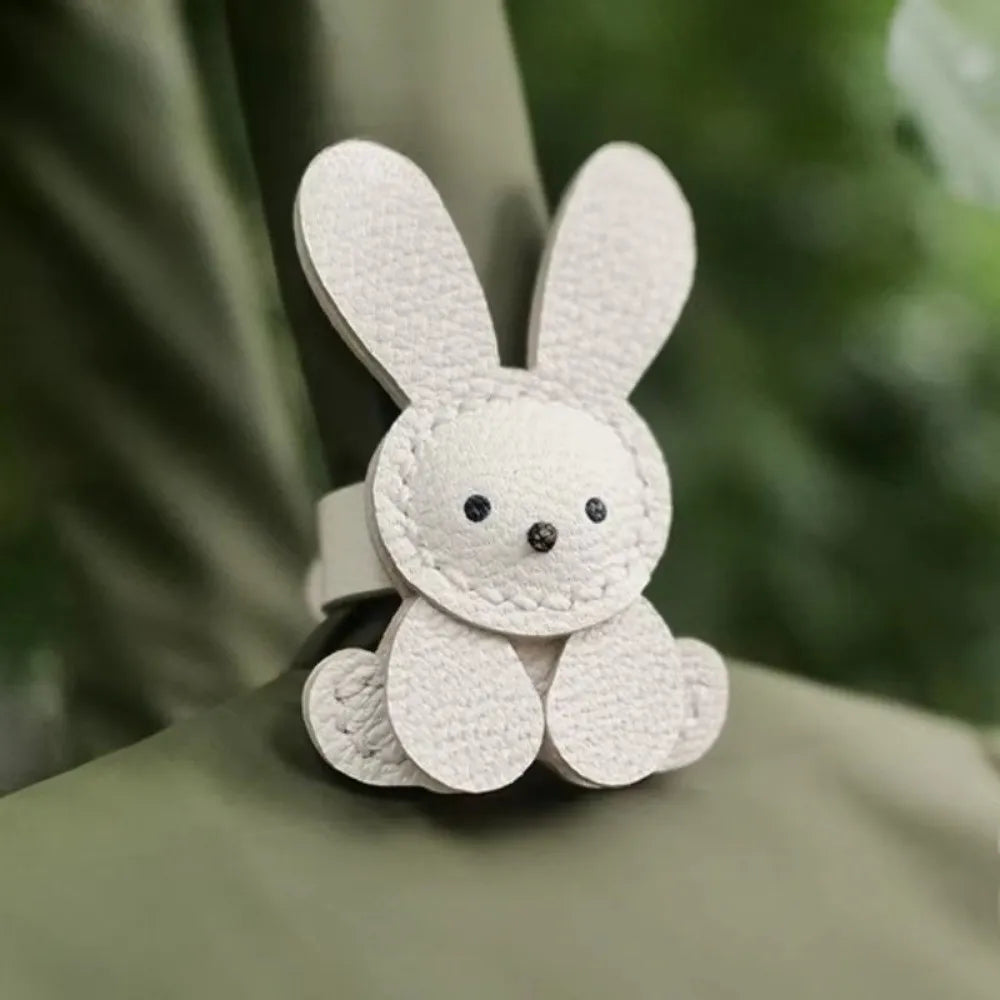 A small, white, embroidered bunny charm attached to a light green fabric.