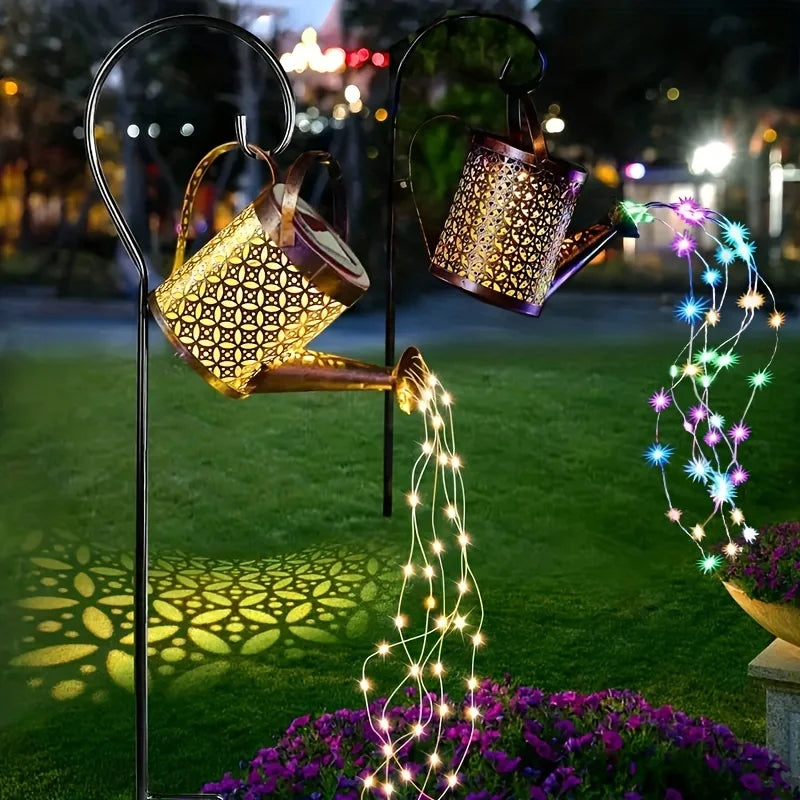 A vintage solar watering can garden light with a shepherd's hook illuminates a cascade of glowing fairy lights over purple fl