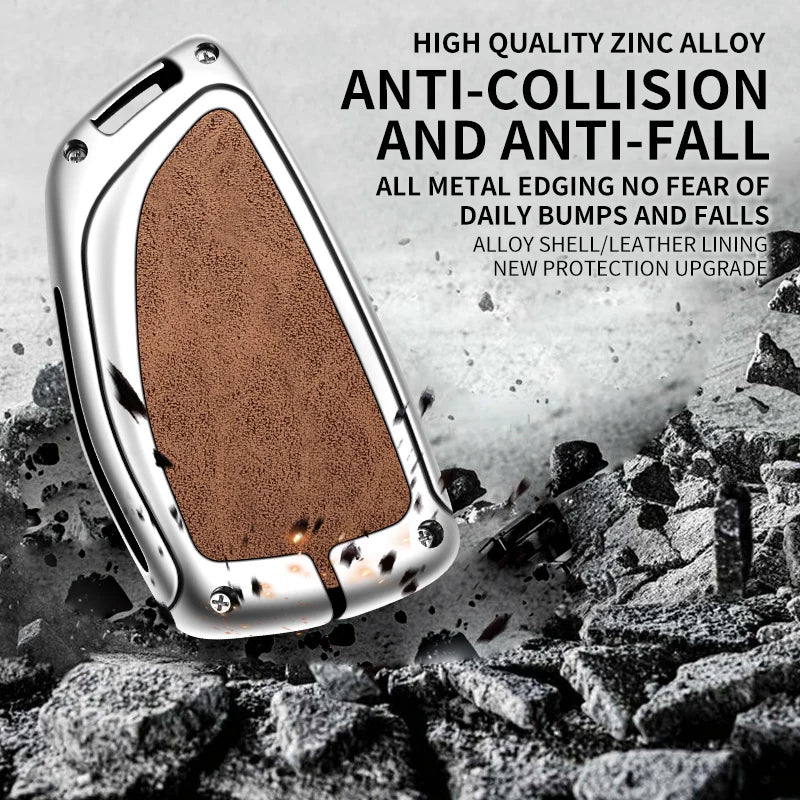A silver zinc alloy car key case with a brown textured finish is shown against a background of scattered black rocks.
