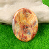 A polished, oval natural crystal stone with swirling shades of orange, red, and yellow rests on green grass.
