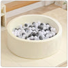 A white plush ball pit playpen filled with various sized gray and white balls on a light wooden floor.