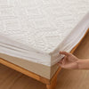 A hand is folding a white quilted mattress protector with extra padding on a wooden bed frame.