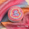 A roll of colorful gradient yarn in pink, orange, and blue tones displayed on a textured fabric.