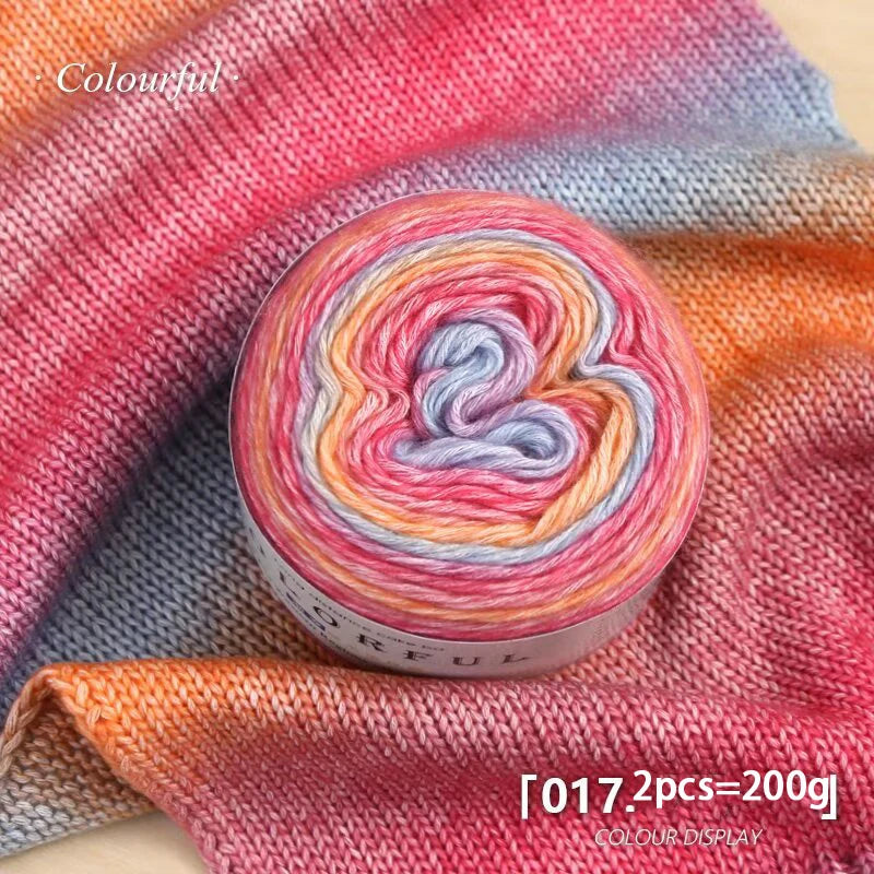 A roll of colorful gradient yarn in pink, orange, and blue tones displayed on a textured fabric.