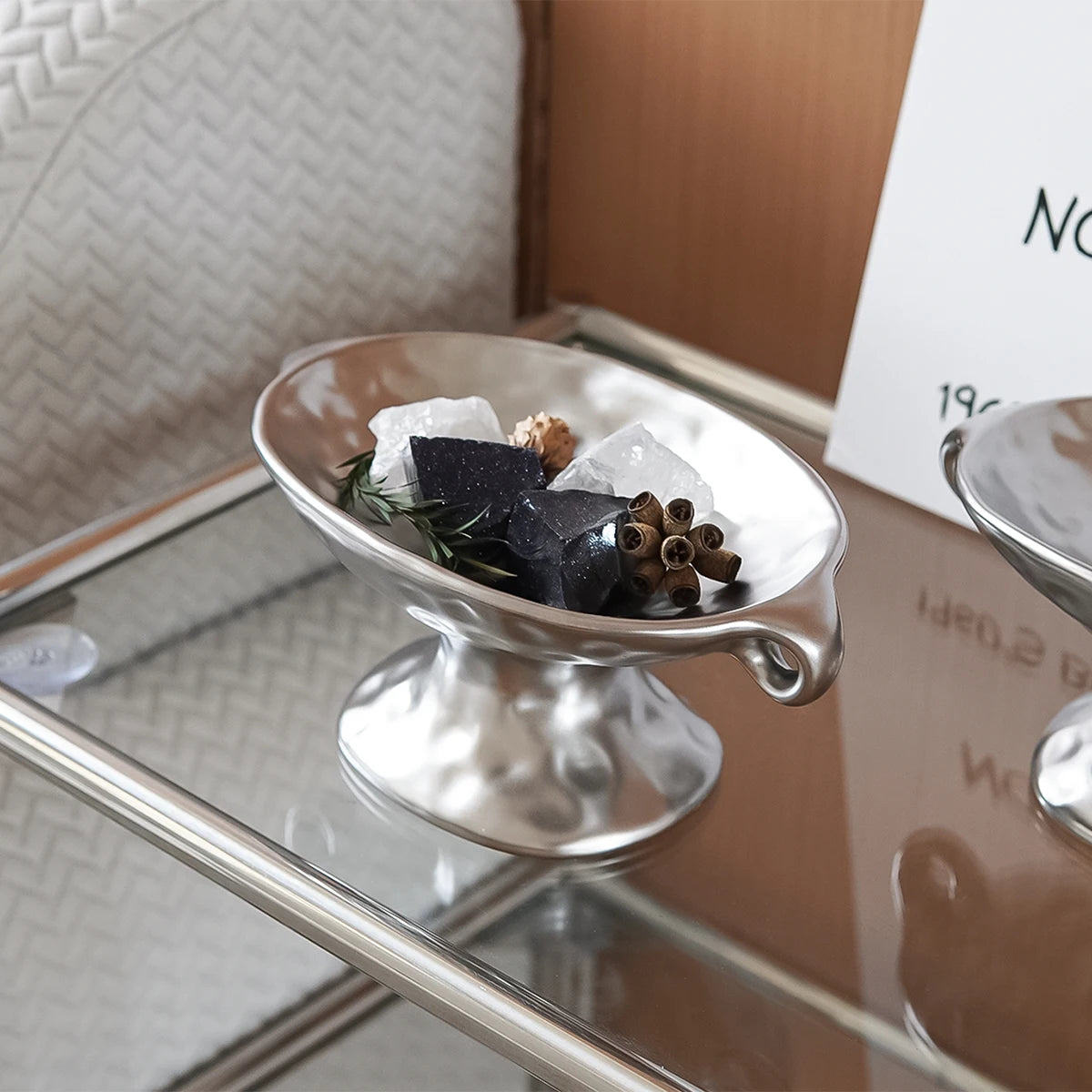A vintage ceramic soap dish with an elevated stand holds several pieces of dark soap and clear ice cubes.