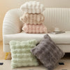 A collection of fluffy decorative pillow covers in cream, beige, and pink resting on a white sofa.