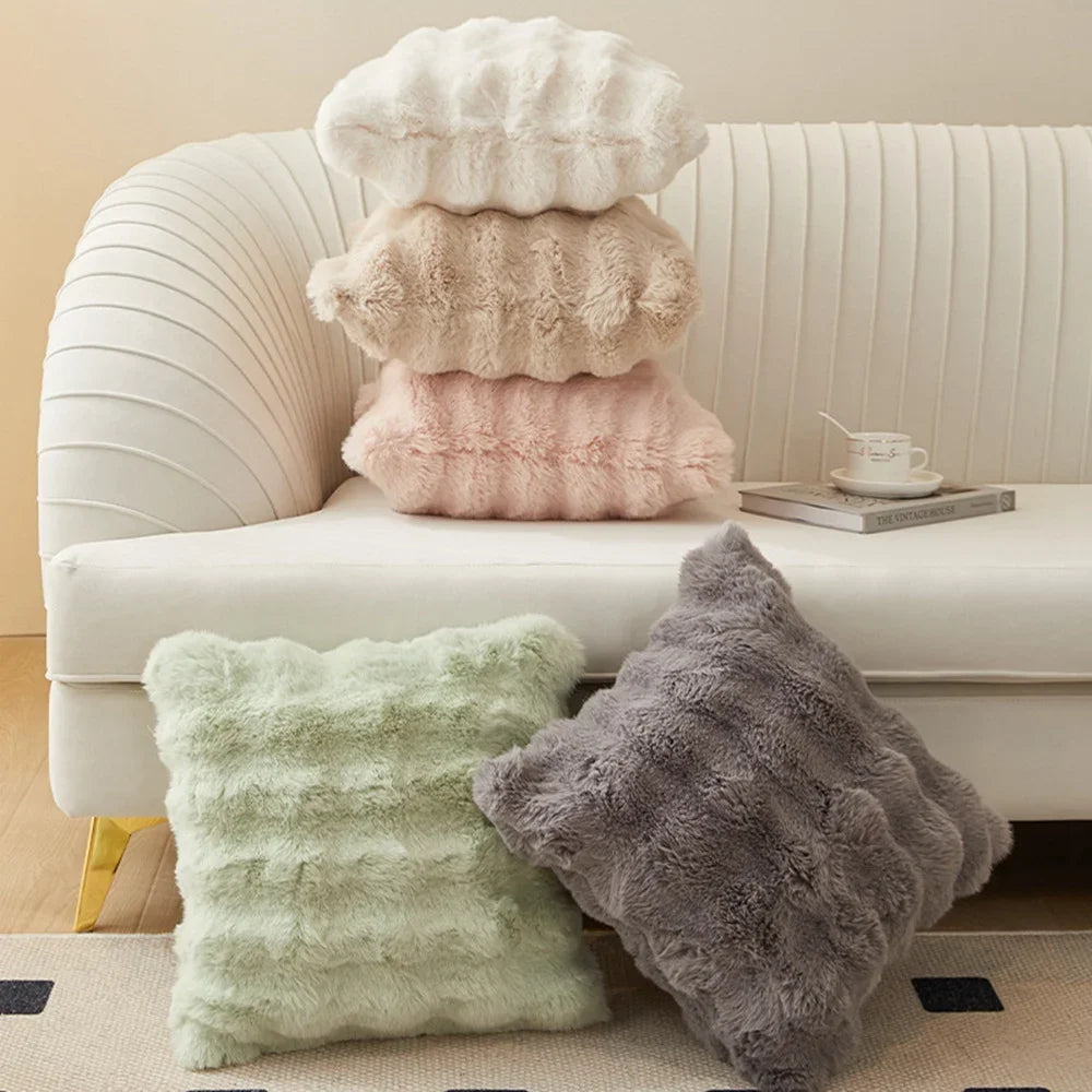A collection of fluffy decorative pillow covers in cream, beige, and pink resting on a white sofa.