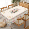 Vintage floral tablecloth set for a dining table with wooden chairs and a potted plant in the background