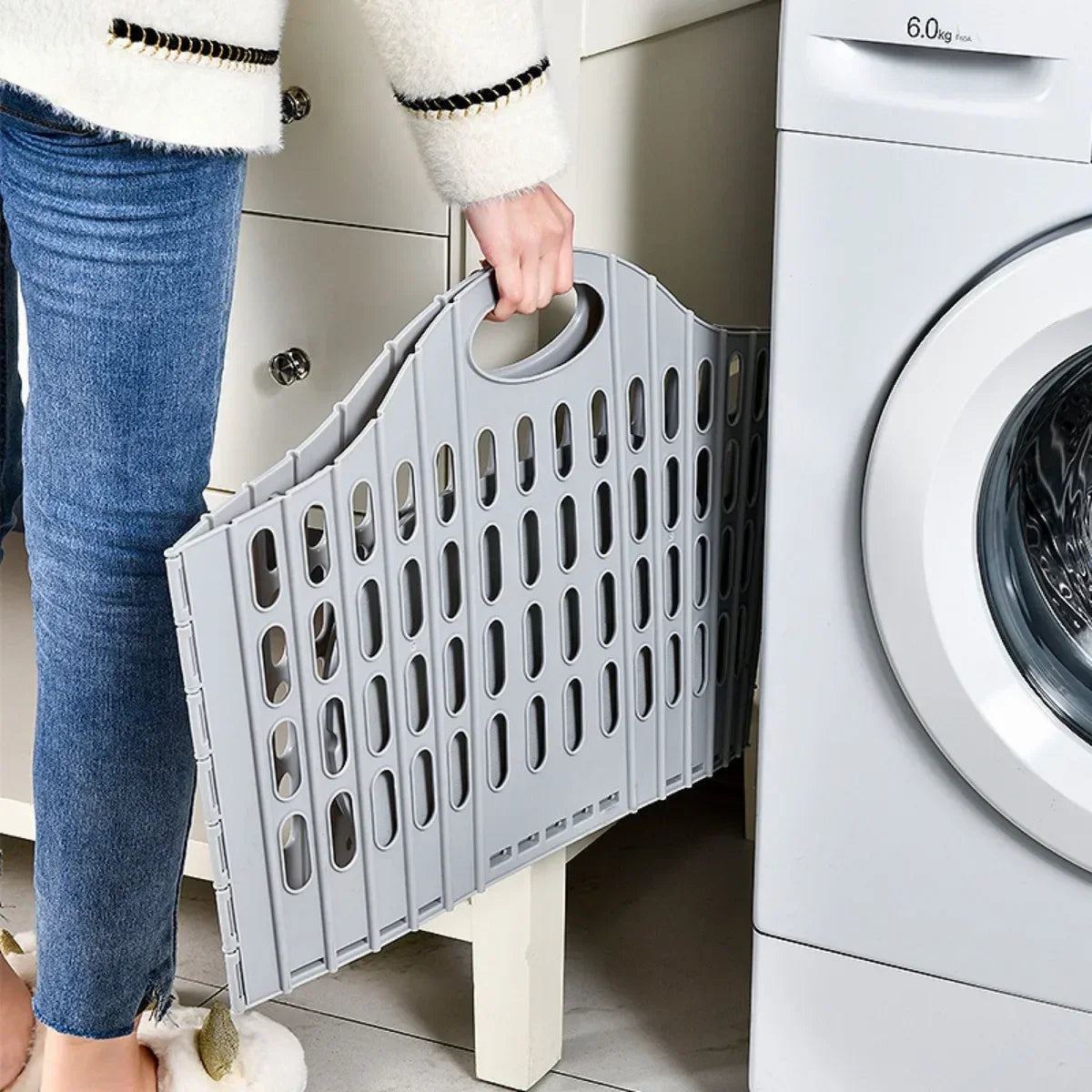 A person is placing a gray modern foldable laundry hamper into a white washing machine.