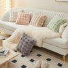 A white sofa is decorated with various soft plush decorative pillow covers in pastel shades and textures.