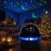 A black spherical projector night light emitting blue and green stars onto a dark room with a starry sky projection.