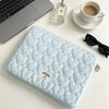 A light blue quilted laptop sleeve with a soft lining resting on a white surface next to a cup and sunglasses.