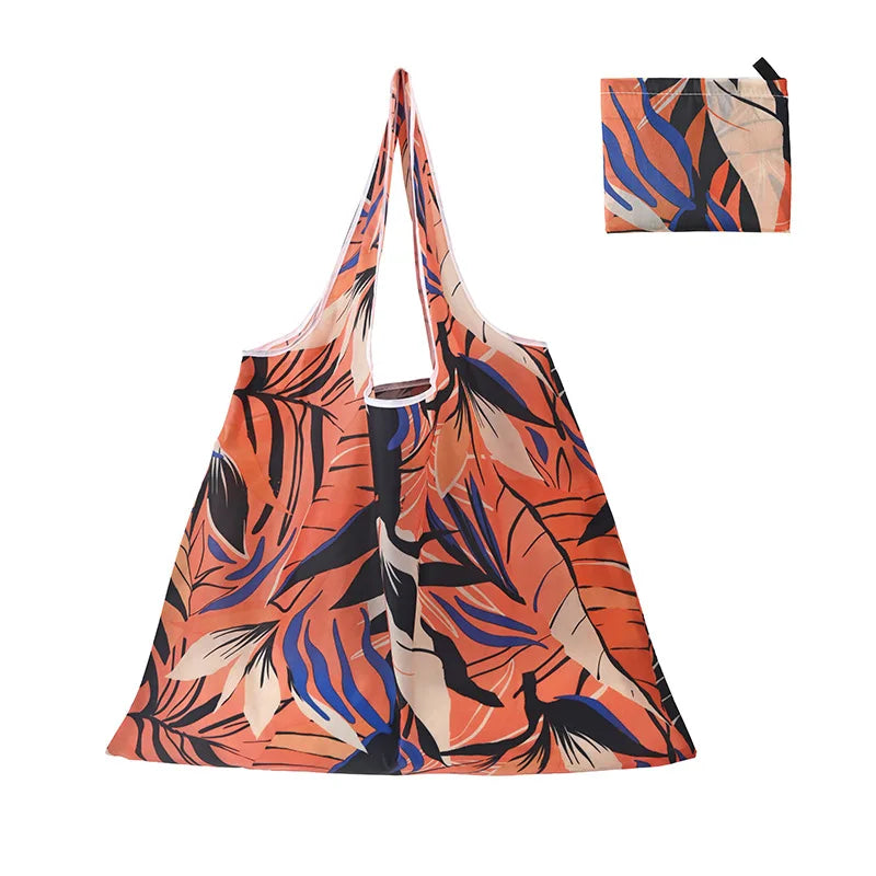 A reusable shopping tote bag featuring an orange and blue tropical leaf print.