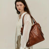A woman models a brown PU leather tote bag with a detachable strap and a white shirt.