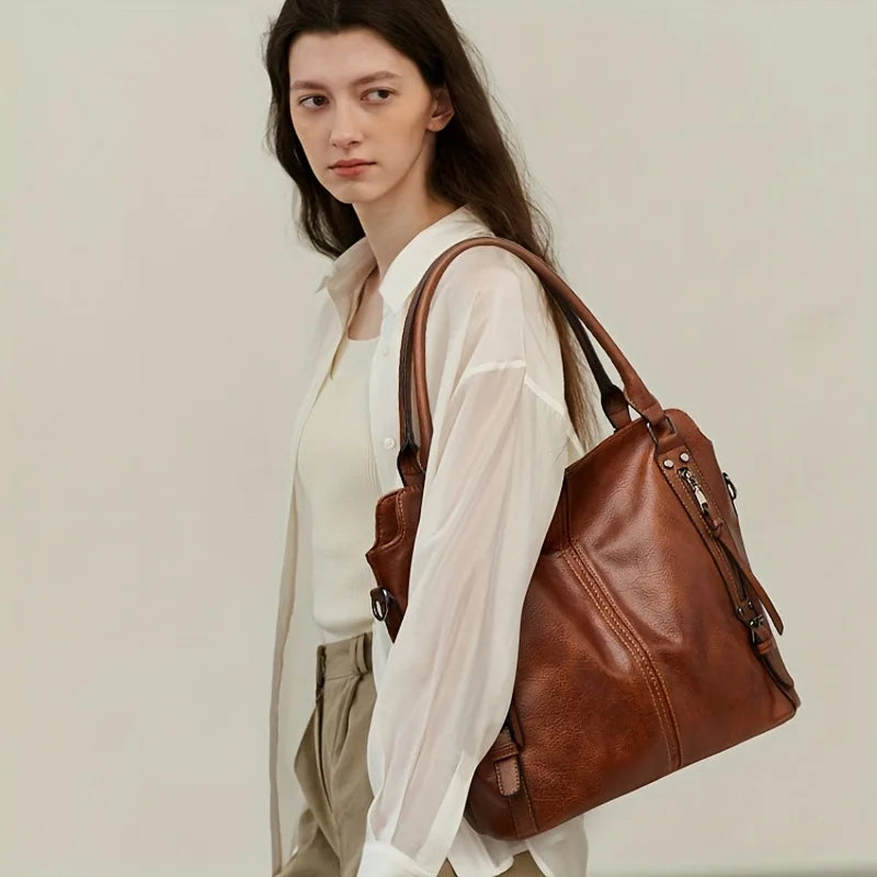 A woman models a brown PU leather tote bag with a detachable strap and a white shirt.