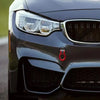Close-up of a dark gray car's front grille and headlight with a red decorative accent.
