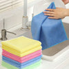 A hand is wiping a blue microfiber cleaning cloth on a kitchen sink, with stacks of colorful cleaning cloths nearby.