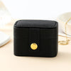 A black compact leather jewelry travel case with a gold accent is shown on a light surface.