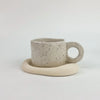 A ceramic coffee mug with a speckled beige glaze resting on a matching silicone coaster.