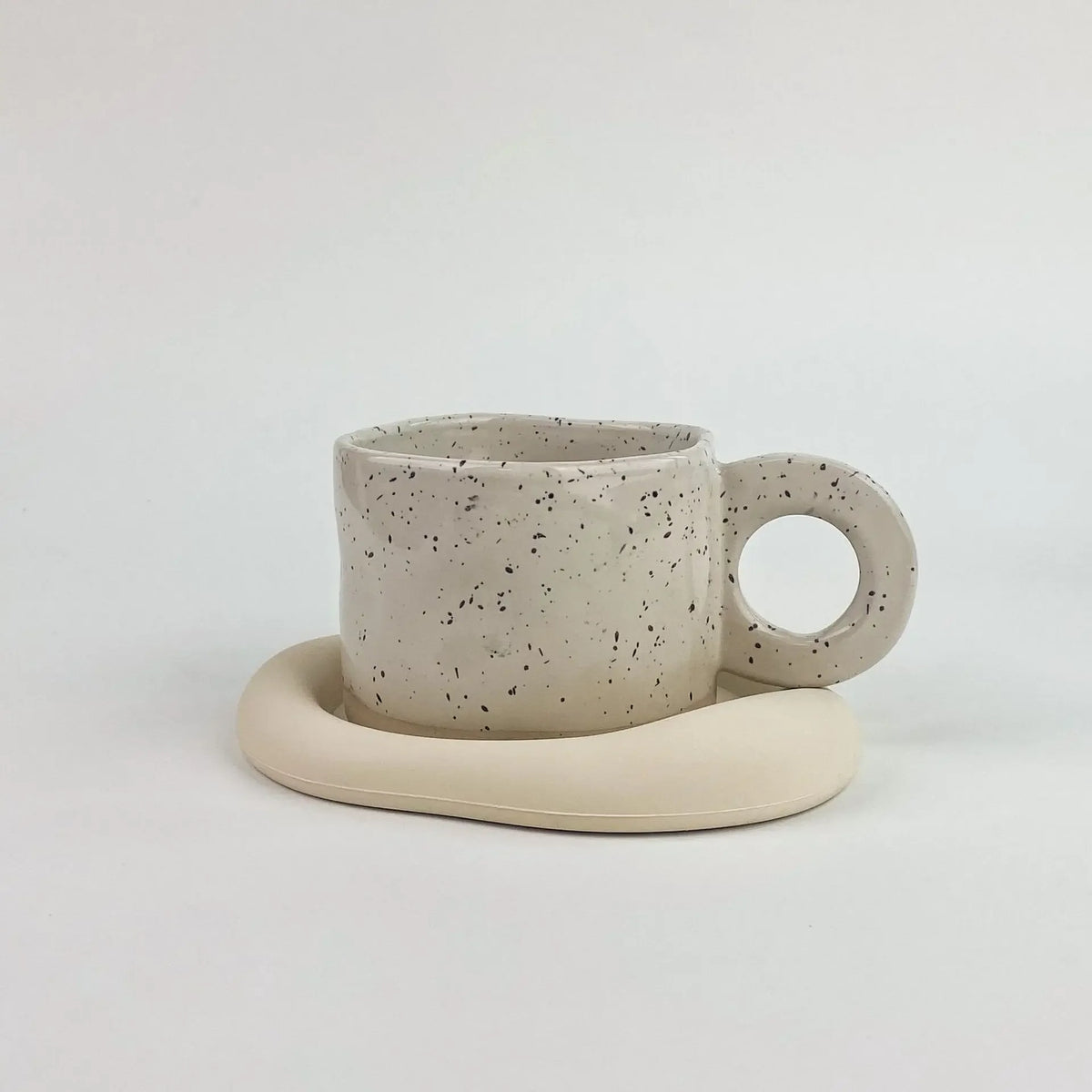 A ceramic coffee mug with a speckled beige glaze resting on a matching silicone coaster.