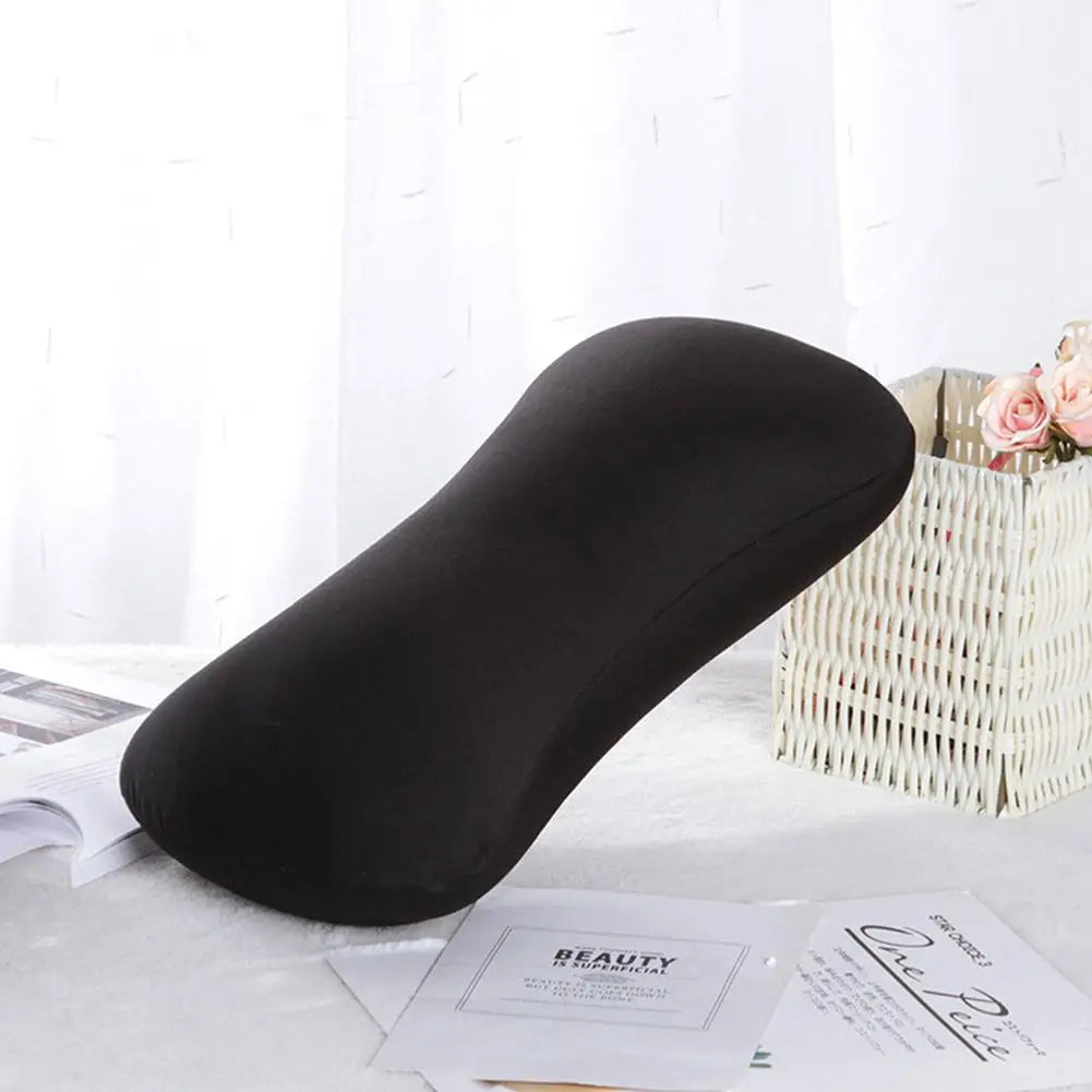 A black microbead bolster pillow is shown resting on a white surface next to a woven basket and some paper.