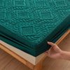 A teal quilted mattress protector with a textured pattern is shown being folded on a wooden surface.