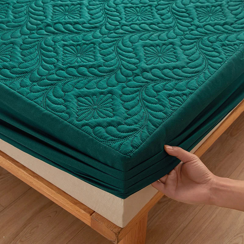 A teal quilted mattress protector with a textured pattern is shown being folded on a wooden surface.