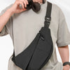 A person wearing a light gray t-shirt is carrying a black practical chest bag with a strap over their shoulder.