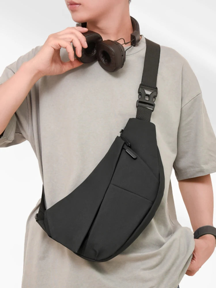 A person wearing a light gray t-shirt is carrying a black practical chest bag with a strap over their shoulder.