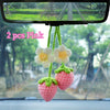 Two pink handmade crochet strawberry pendants hanging from a mirror