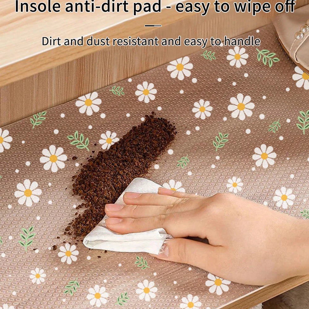 A hand wipes dirt off an insole anti-dirt pad used as a kitchen drawer mat with daisy flower patterns.