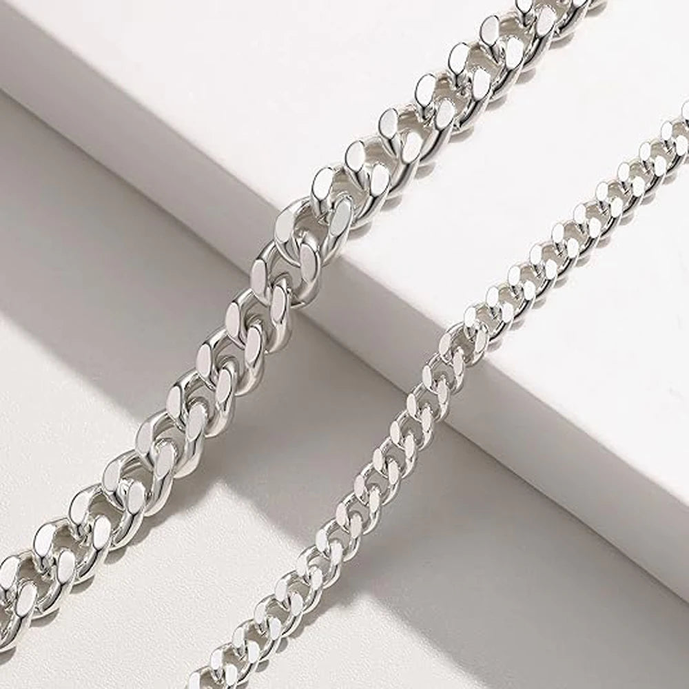Un paire de bracelets de cheville en chaîne cubaine argentée sur une surface blanche.