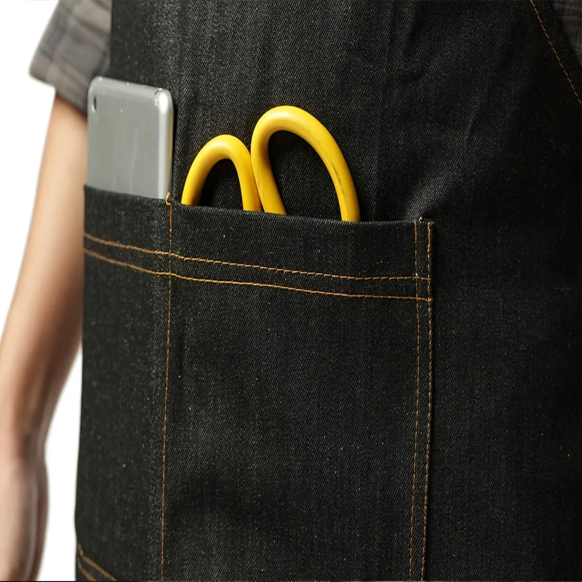 A black denim work apron pocket holds a silver smartphone and two yellow metal rings.