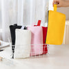 A hand is holding a bright yellow canvas zipper pouch next to several pink and red pouches in a white wire basket.