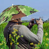 Une personne portant un chapeau parapluie camouflage prend une photo à l'extérieur dans un champ herbeux.