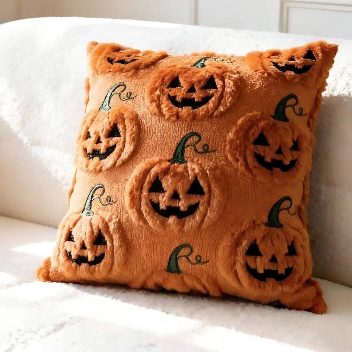 A plush throw pillow covered in an orange fabric featuring repeating carved jack-o'-lanterns and green maple leaves.