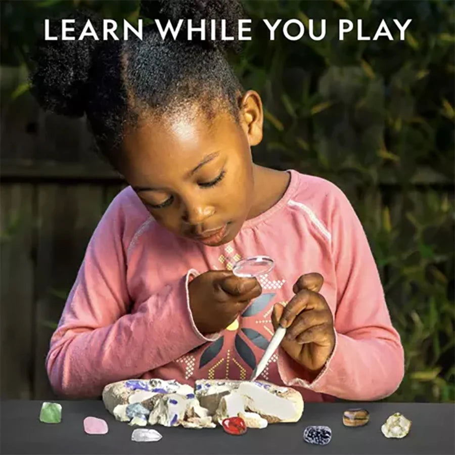A young girl is excavating gemstones and crystals from a rock using a kit, learning while playing.