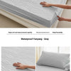 Gray waterproof fitted mattress protector being demonstrated, showing its soft texture and fit.