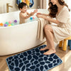 A woman is sitting by a bathtub with a child, and a dark blue pebble texture bathroom mat is placed on the floor.