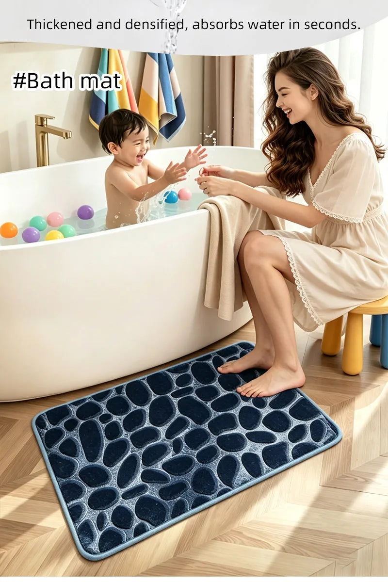 A woman is sitting by a bathtub with a child, and a dark blue pebble texture bathroom mat is placed on the floor.