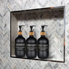 Three black refillable soap dispenser bottles for shampoo, conditioner, and body wash displayed in a modern bathroom shelf.