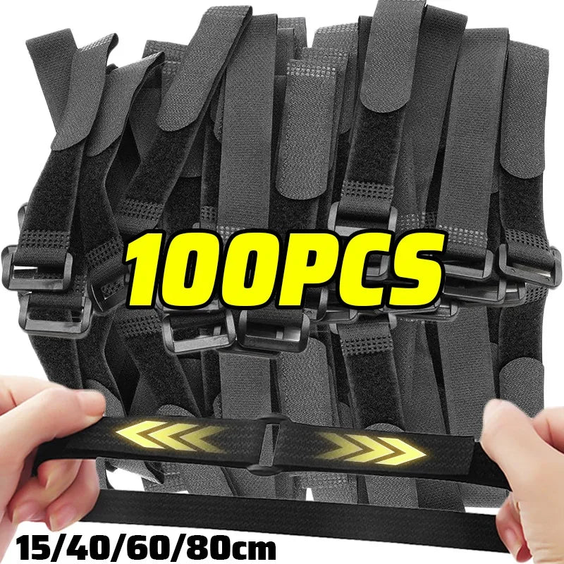 A hand is holding a bundle of black reusable nylon cable ties with adjustable hook and loop fasteners.