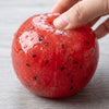 Une main serre un jouet anti-stress en watermelon rouge vif, montrant sa texture moelleuse.