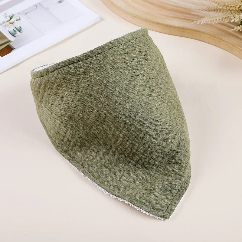 A soft olive green cotton baby bib is shown lying on a light surface.