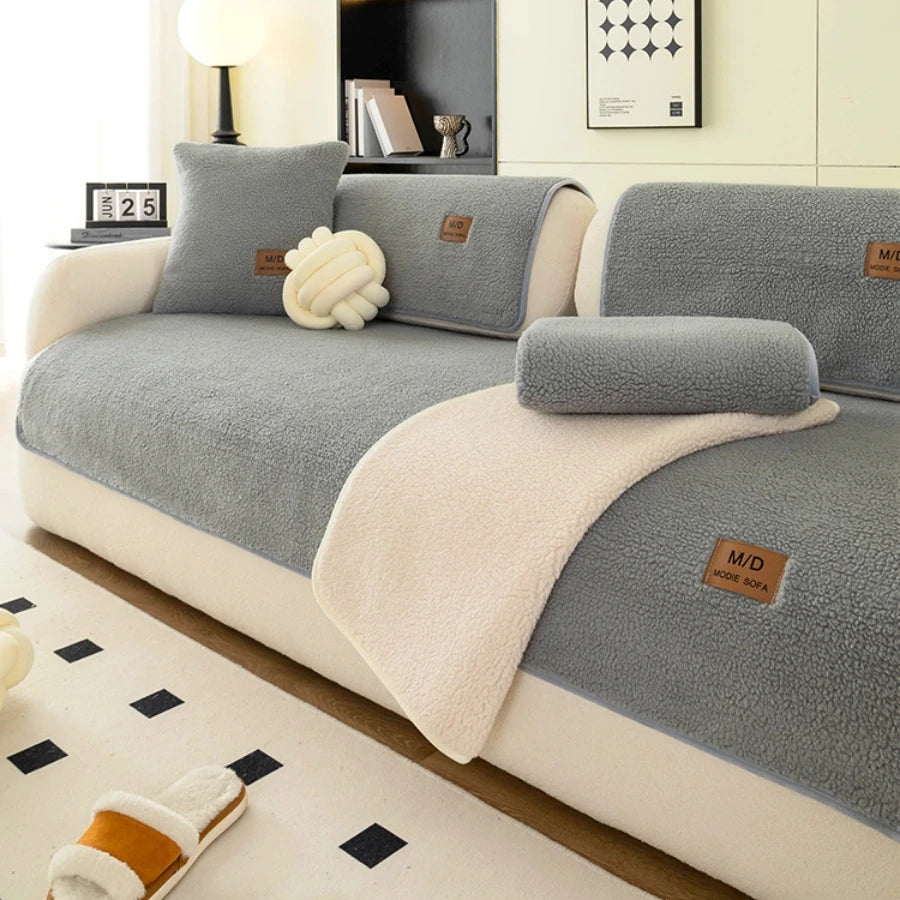 Housse de canapé sherpa grise avec accents beige clair et coussins, exposée sur un canapé de salon.