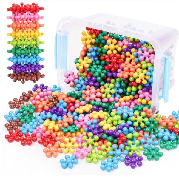 A clear container filled with colorful snowflake interlocking building blocks scattered on a white surface.
