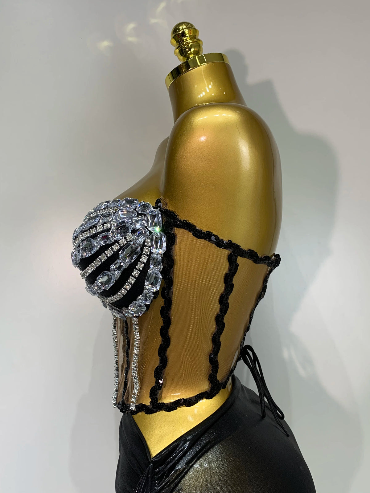 A gold mannequin displays a sparkly two-piece party outfit with a see-through top and black detailing.