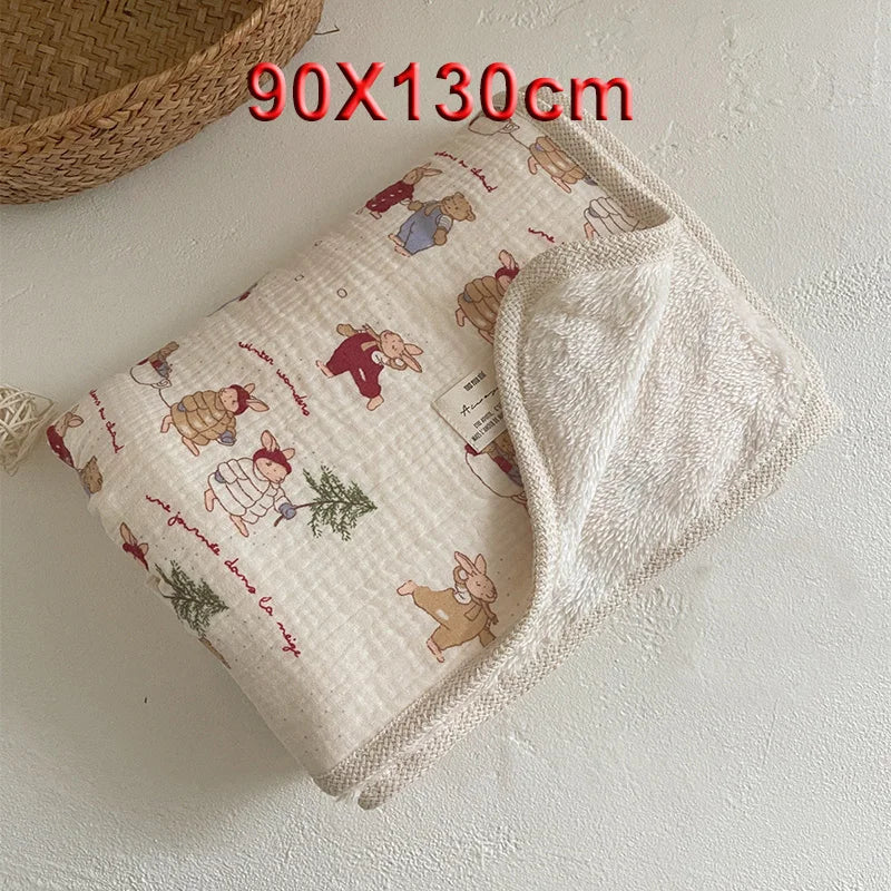 A folded floral muslin baby blanket with embroidered animals and a white cotton swaddle visible on a light surface.